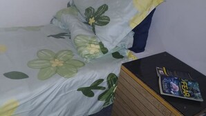 Pieni huone, jossa on yksi sänky, kukallinen päiväpeite ja yöpöytä, jonka päällä on kirja.