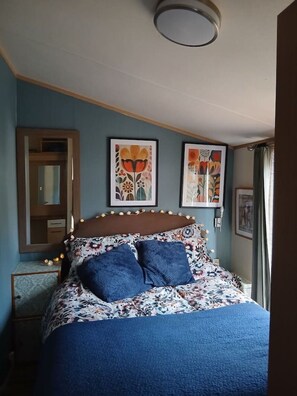 Een slaapkamer met een bed, een spiegel en twee wanddecoraties met bloemen.