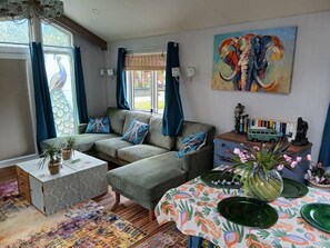 A living room with a sofa, coffee table, and a dining table with green plates. - Peacock Lodge Quirky & Tranquil Home Away from Home (Perth and Kinross)