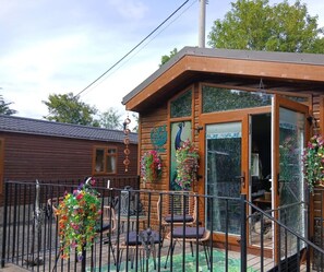 A wooden cabin with a glass door, a balcony with wicker furniture, and hanging flower baskets.