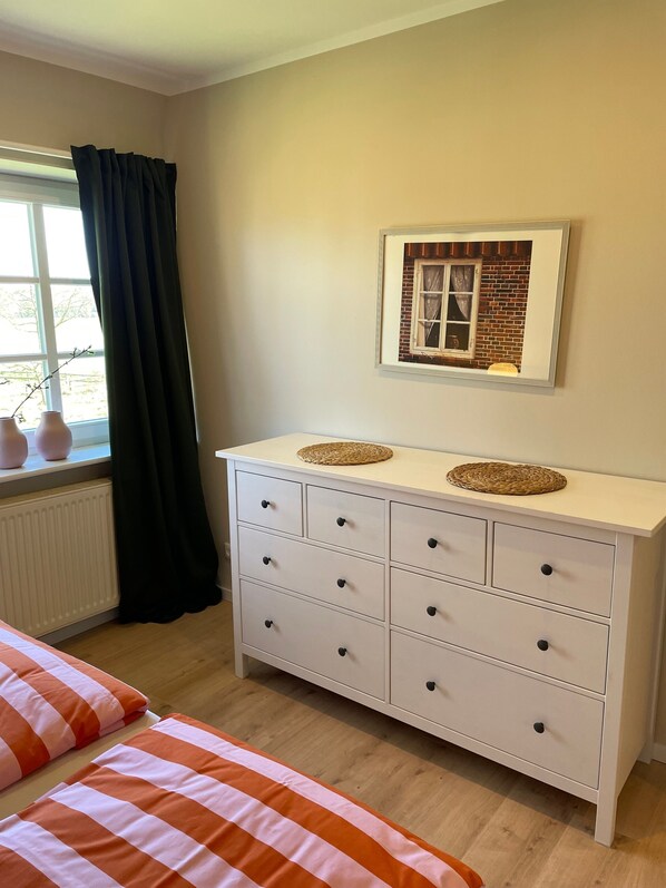 A bedroom with a white dresser, a framed picture on the wall, and a window with curtains.