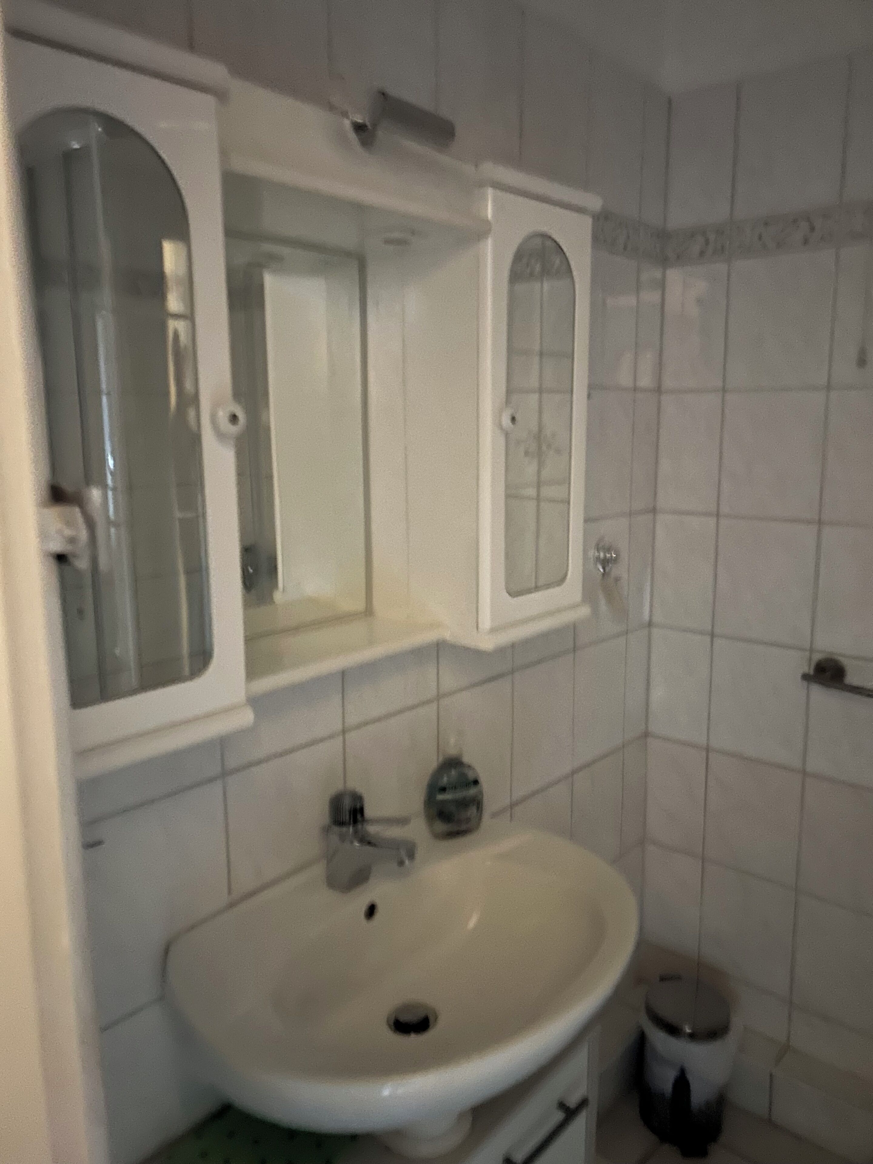 Kylpyhuone, jossa on valkoinen pesuallas, peili ja wc-istuin.