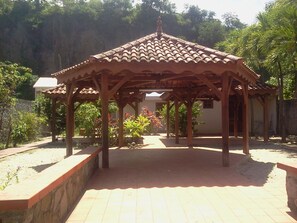 A wooden gazebo with a tiled roof, surrounded by plants and trees.