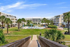 A resort with a pool area, palm trees, and a wooden walkway leading to the buildings.