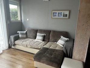 A room with a sofa, a wooden floor, and a window. - Small house with air conditioning and a small garden (Frontignan)