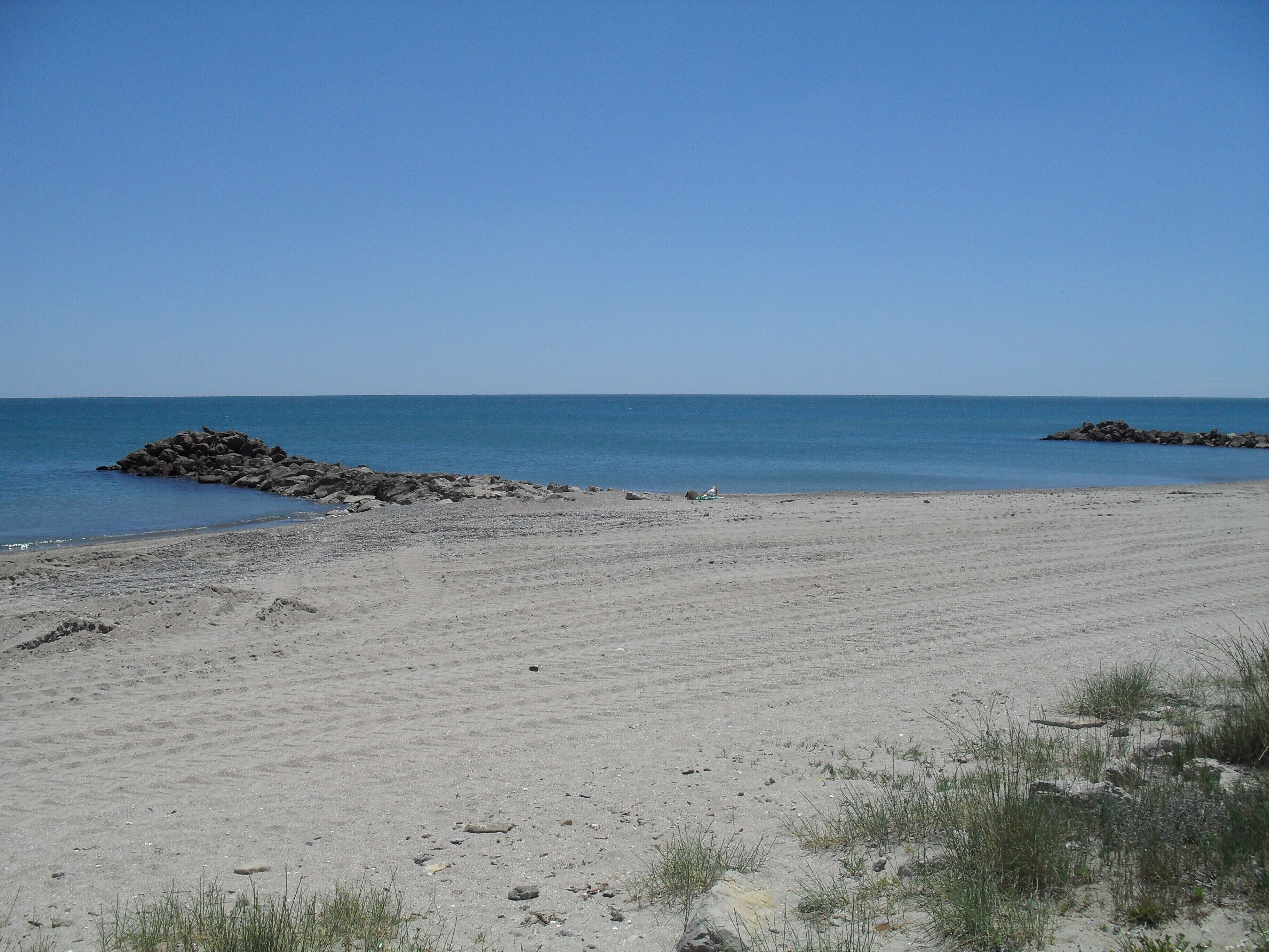 A beach with a clear sky, calm sea, and rocky outcrops.