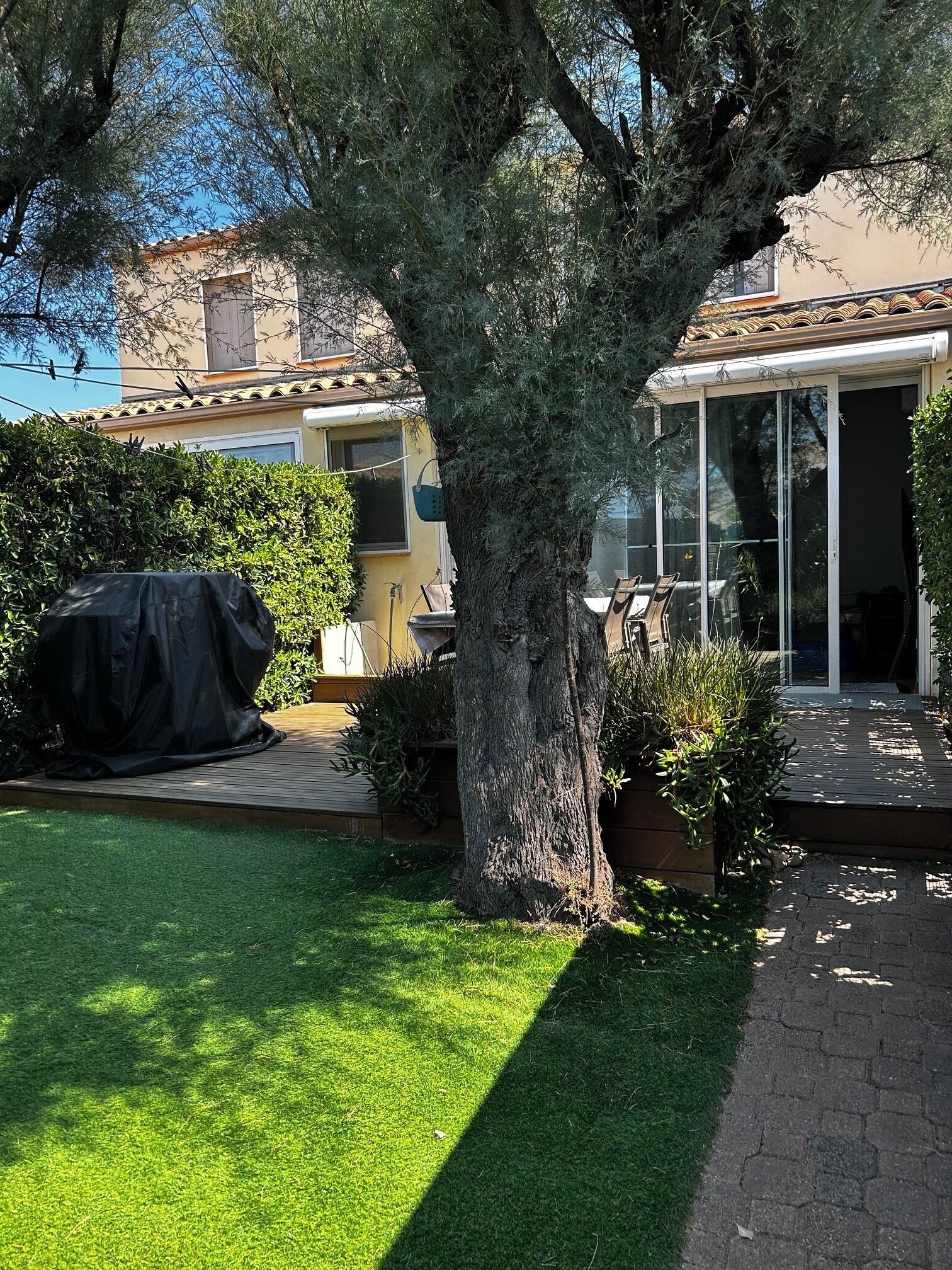 A residential property with a large tree, a covered patio, and a house with a tiled roof.