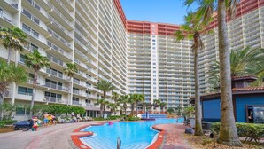 A hotel with a swimming pool, palm trees, and a multi-story building. - High Tide Hideaway at Shores of Panama #1918 - Oceanfront, High-Rise, Pools, Covered Parking (Panama City Beach)