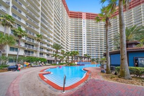 A hotel with a swimming pool, palm trees, and a multi-story building. - High Tide Hideaway at Shores of Panama #1918 - Oceanfront, High-Rise, Pools, Covered Parking (Panama City Beach)