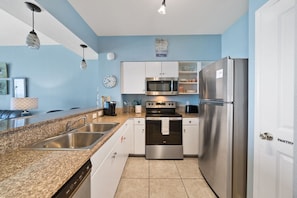 A modern kitchen with granite countertops, stainless steel appliances, and a clock on the wall. - High Tide Hideaway at Shores of Panama #1918 - Oceanfront, High-Rise, Pools, Covered Parking (Panama City Beach)