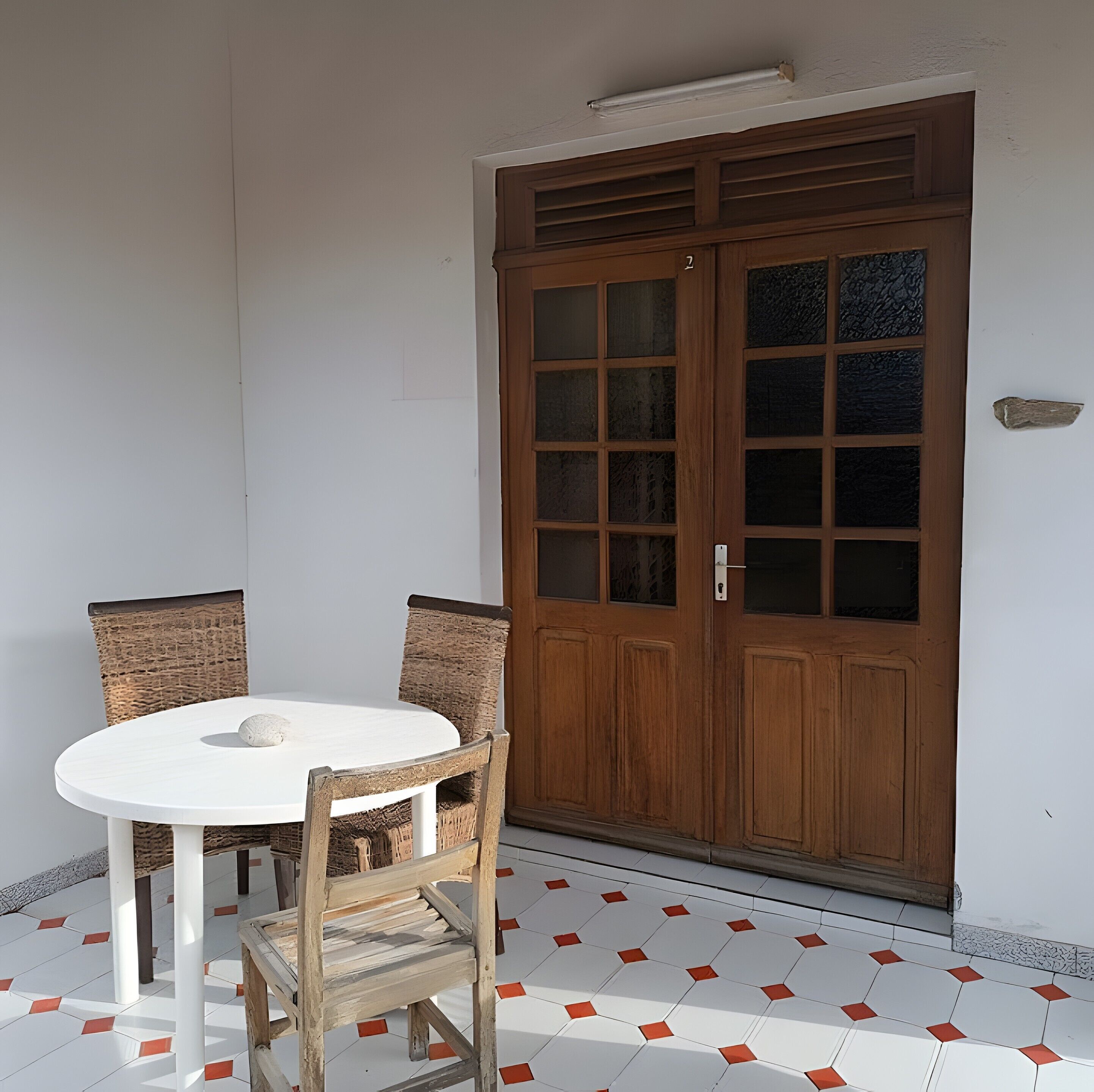 Une table ronde avec deux chaises, une porte en bois dotée de panneaux de verre et un sol carrelé orné d’un motif géométrique.