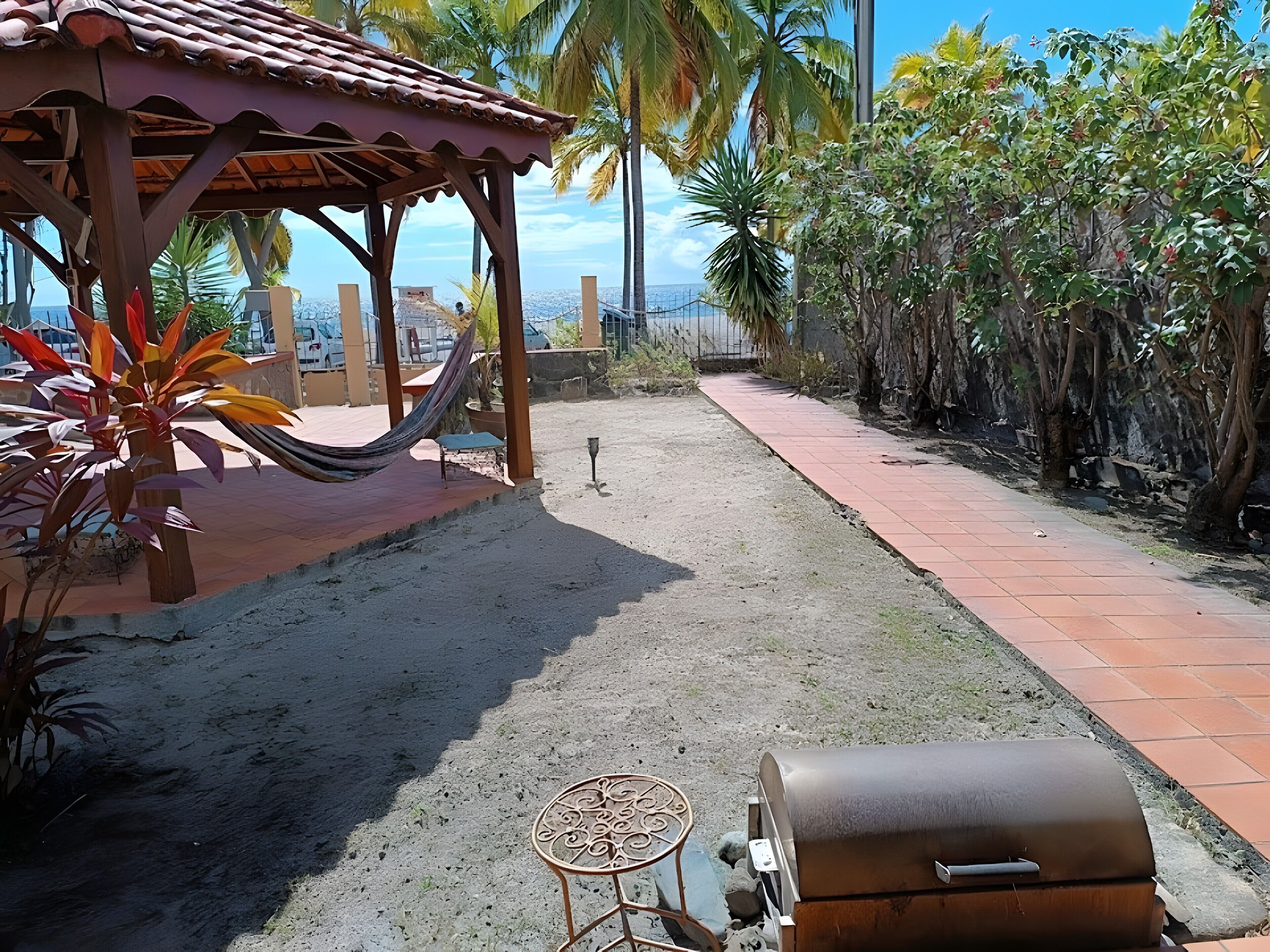 Une terrasse avec un hamac, un barbecue et une petite table.