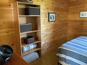 Una habitación con paneles de madera, una cama, una estantería y un ventilador.