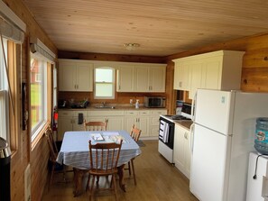 Eine kompakte Küche mit Holzschränken, einem Esstisch mit Stühlen, einem Kühlschrank und einer Mikrowelle.