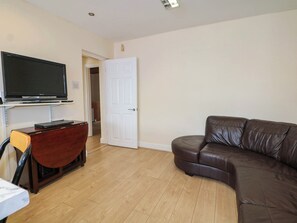 A living room with a brown leather sofa, a flat-screen TV mounted on the wall, and a wooden cabinet. - 90 A Station Road (New Milton)