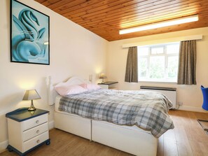 A bedroom with a bed, bedside tables, a lamp, a window with curtains, and a painting on the wall. - 90 A Station Road (New Milton)
