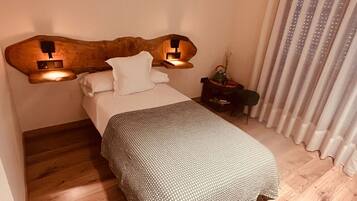 Une chambre à coucher avec une tête de lit en bois, un lit avec une literie blanche, une table de chevet avec une lampe et une fenêtre avec des rideaux.