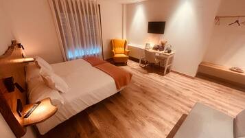 Habitación de hotel con cama, mesita de noche, lámpara, silla, escritorio y televisor montado en la pared.