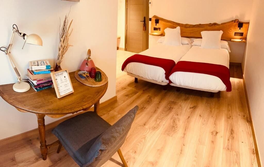 A bedroom with a wooden headboard, a bedside table with books and a lamp, and a red blanket on the bed.
