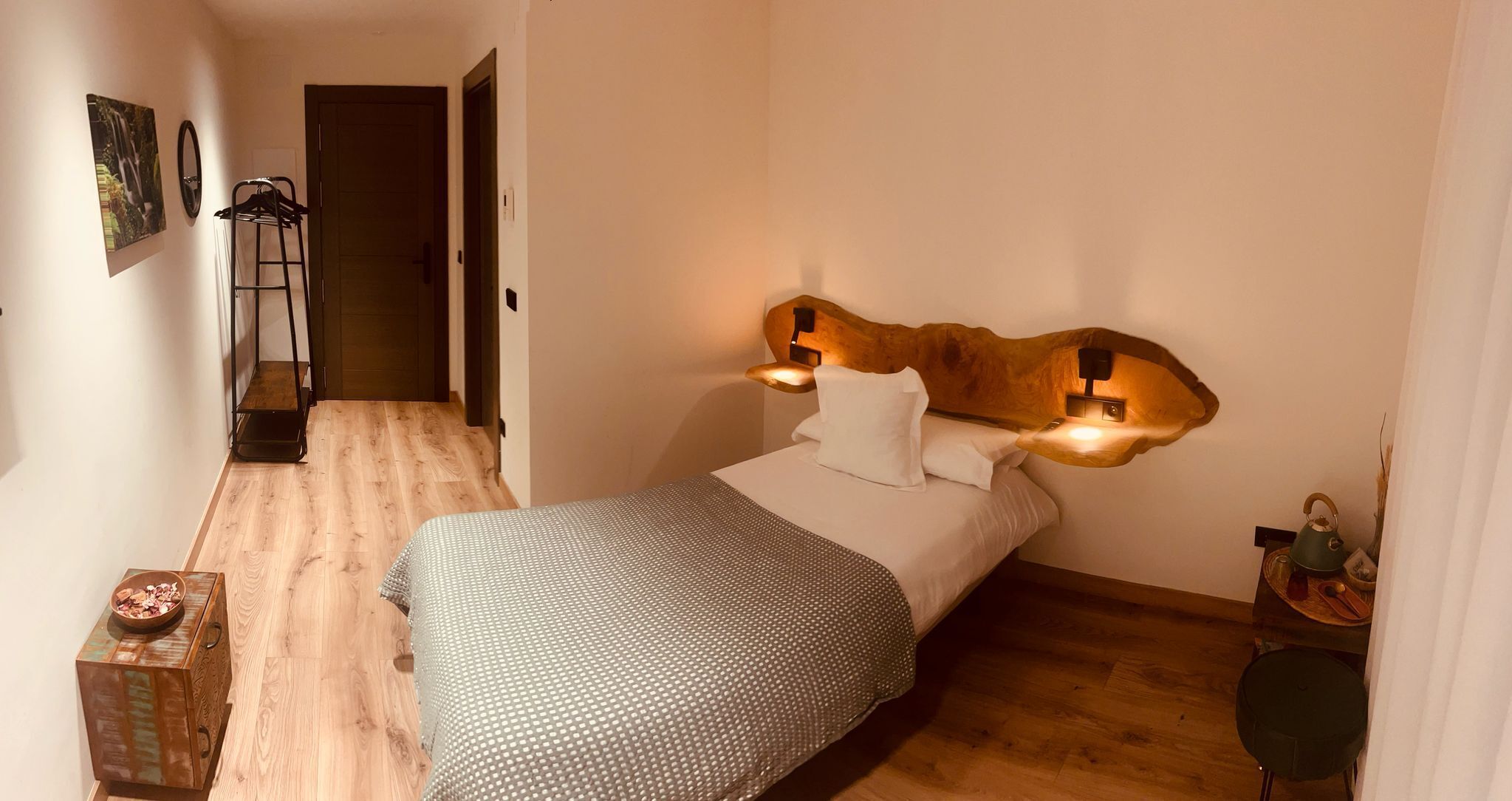 Une chambre à coucher avec un lit, une tête de lit en bois, une table de chevet et une petite table sur laquelle se trouve un bol.