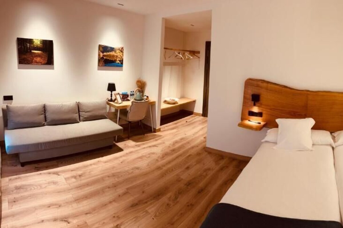A modern bedroom with a wooden headboard, a double bed, a sofa, a desk, and a chair.
