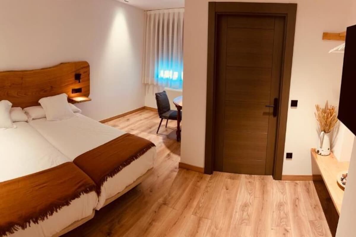 A hotel room with a large bed, a wooden headboard, a desk with a chair, a door, and a television on the wall.