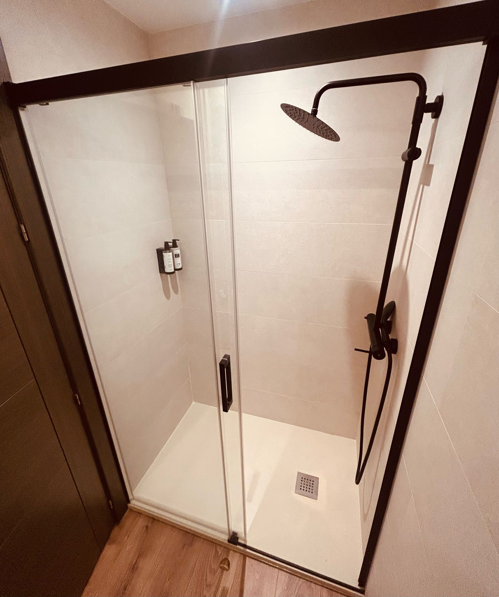 Una cabina de ducha con paredes de vidrio, un cabezal de ducha manual y un control manual.