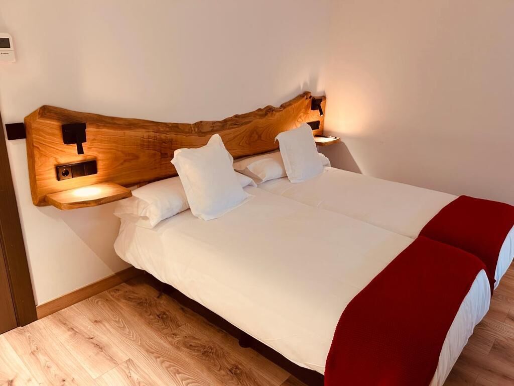 Cama com cabeceira de madeira, roupa de cama branca e duas luminárias laterais.