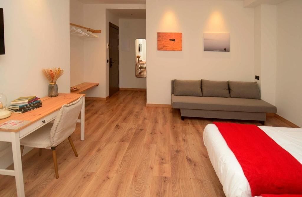 Een kamer met een bed, een bank, een bureau en een stoel. Twee wandlampen en een schilderij aan de muur.
