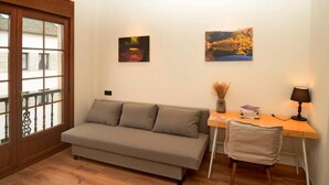 A room with a sofa, a desk, a chair, and two framed pictures on the wall.
