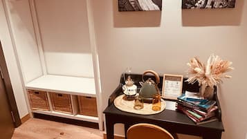 Una habitación con piso de madera, una mesa negra con una silla, un juego de té, un cartel de bienvenida y dos cuadros en la pared.