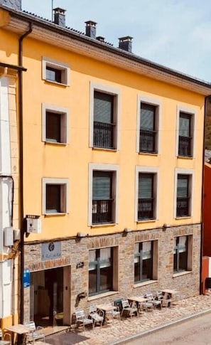 A yellow building with multiple windows and a ground-level outdoor seating area. - A Reigada Hotel Restaurante (Grandas de Salime)