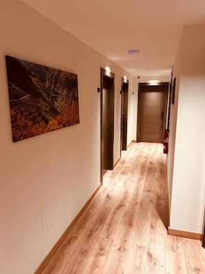 A hallway with wooden flooring, a painting on the wall, and a door at the end. - A Reigada Hotel Restaurante (Grandas de Salime)
