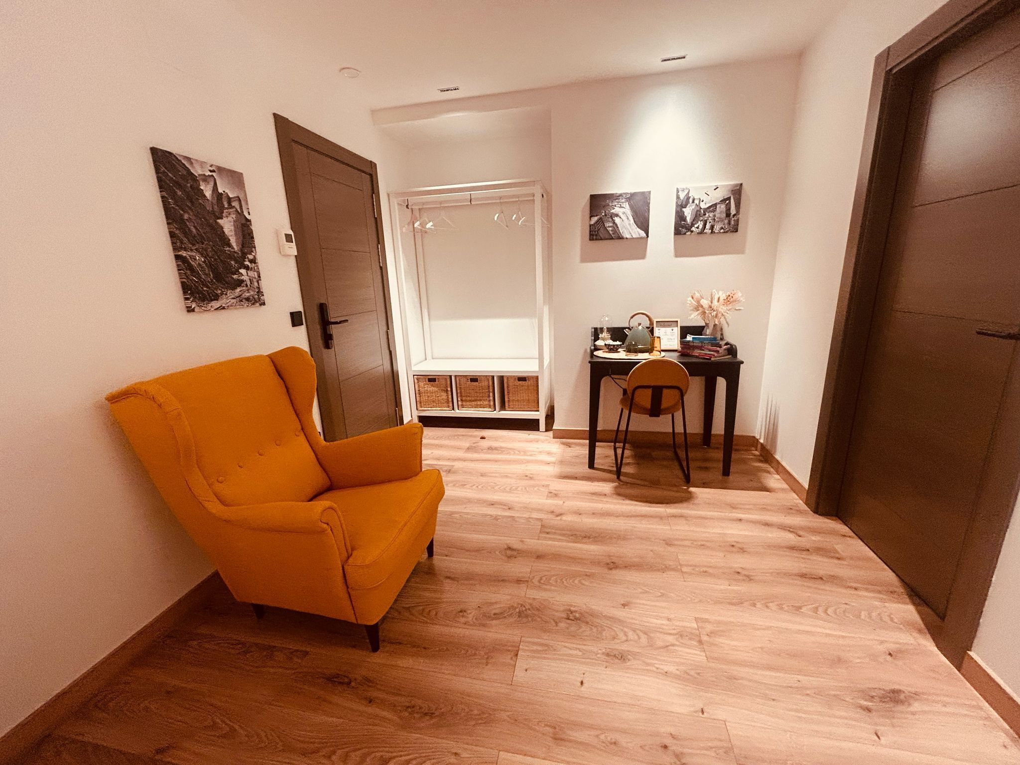 A hallway with a wooden floor, a yellow armchair, a small table with a chair, and a door.