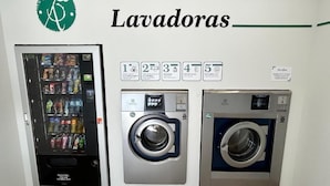 A laundromat with a vending machine, a washing machine, and a dryer, along with a sign indicating the number of machines available.