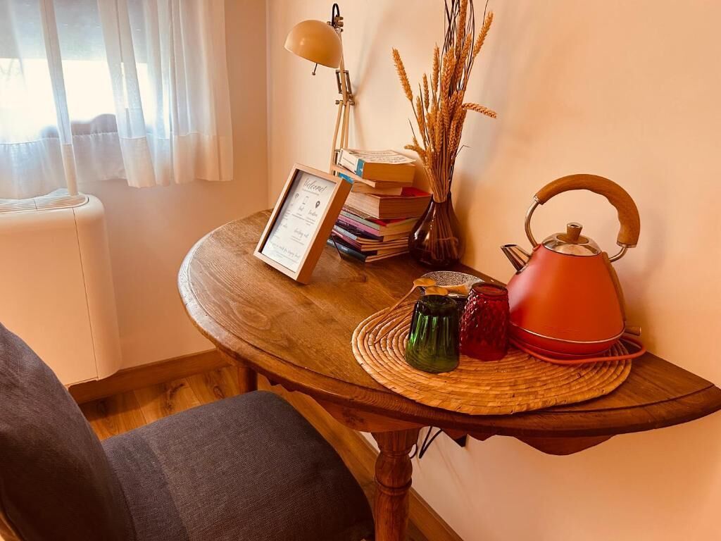Une table en bois sur laquelle sont posés un certificat encadré, une bouilloire rouge, une lampe et divers objets décoratifs.