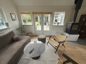 Ein modernes Wohnzimmer mit einer Couch, einem runden Couchtisch und einem Korbstuhl. Ein Kamin und ein Fenster mit Blick ins Freie sind ebenfalls vorhanden.