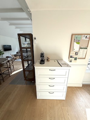 Ein Zimmer mit weißem Schreibtisch, einem Korkwand mit angepinnten Gegenständen, einem Holzstuhl und einem Fernseher an der Wand.
