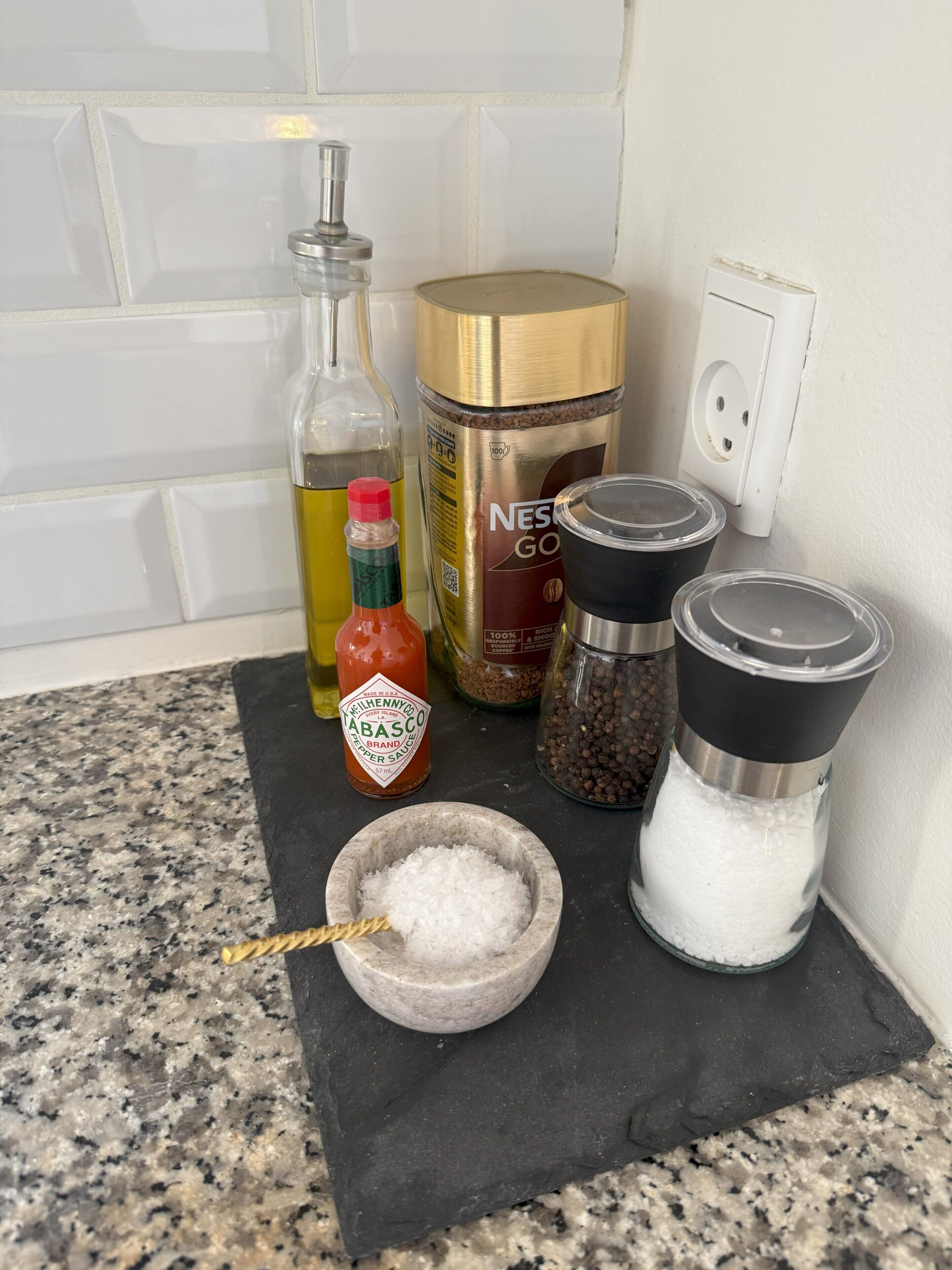 A kitchen counter with various items including a bottle of Tabasco sauce, a container of coffee, pepper grinders, and salt shakers.