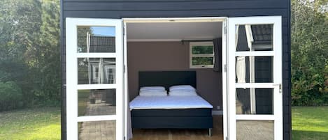 Uma cabana compacta, com um quarto, uma cama, uma pequena janela e uma porta.