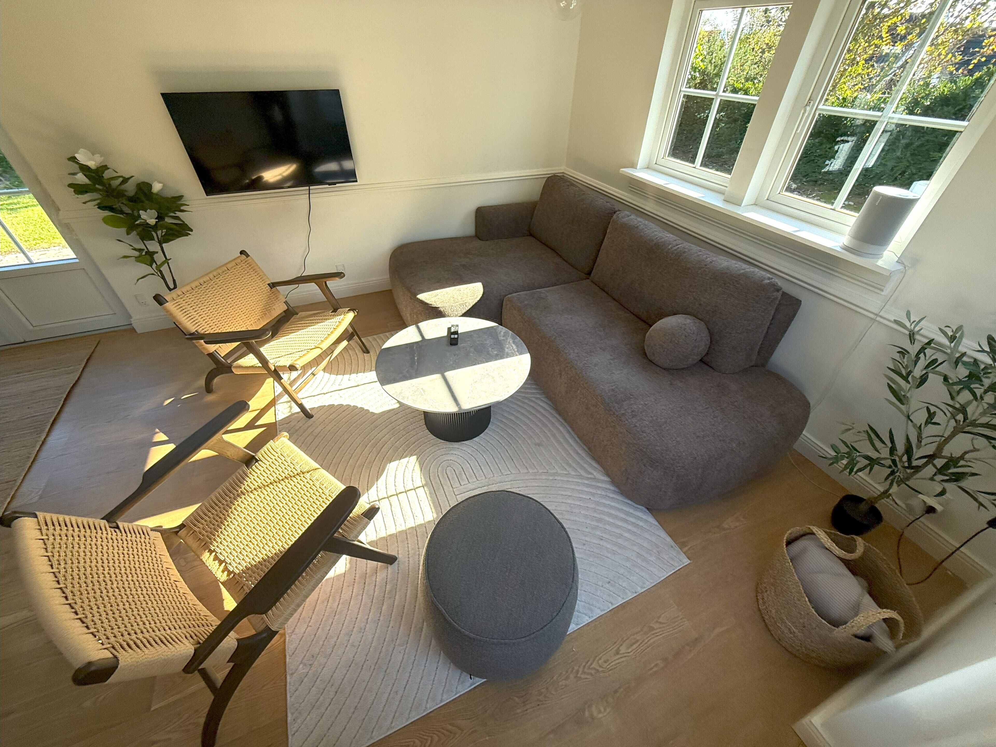 Een woonkamer met een bank, twee fauteuils, een salontafel en een flatscreen televisie aan de muur.