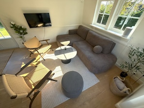 Ein Wohnzimmer mit einer Couch, zwei Sesseln, einem Couchtisch und einem an der Wand befestigten Flachbildfernseher.