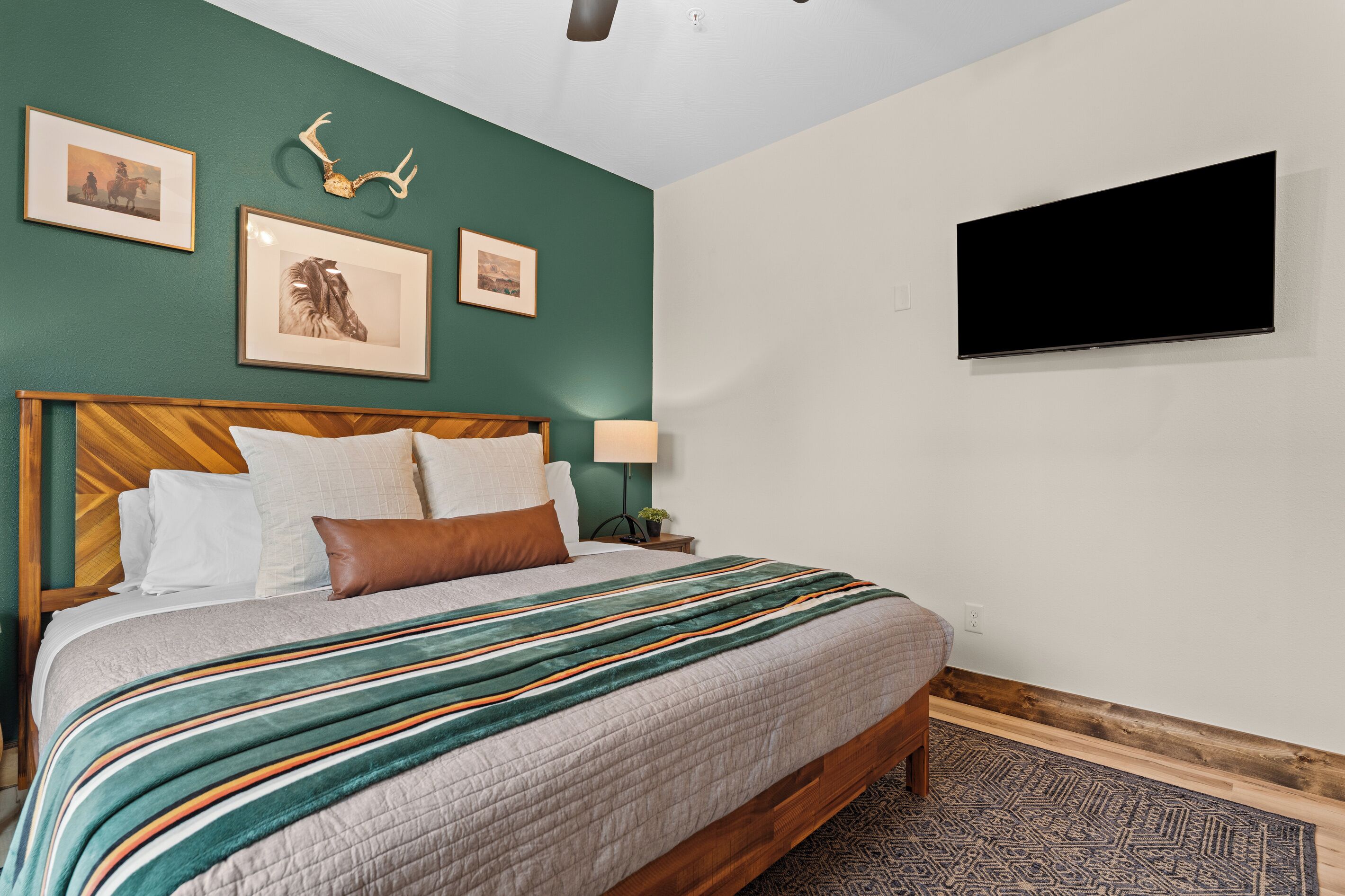 A bedroom with a bed, a mounted TV, framed pictures, and a deer skull on the wall.