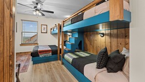 A compact room with bunk beds, a ceiling fan, a window with blinds, and a framed playing card on the wall. - HotTub+Arcade+Pool | 15min to Dolly's Stampede (Hollister)