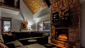 A cozy living room with a stone fireplace, leather sofa, and a ceiling with exposed wooden beams. - HotTub+Arcade+Pool | 15min to Dolly's Stampede (Hollister)