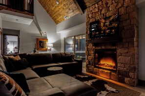 Ein gemütliches Wohnzimmer mit Kamin aus Stein, Ledersofa und einer Decke mit freiliegenden Holzbalken.