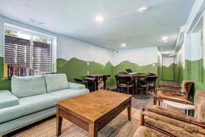 A room with a green wall mural, a sofa, a coffee table, a dining table with chairs, and a window with blinds. - Aloha Springs! Private Heated Pool & Hot Tub (Colorado Springs)