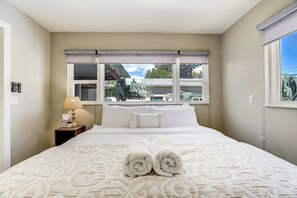 Ein Hotelzimmer mit einem großen Bett, einem Nachttisch mit Lampe und einem Fenster mit Blick ins Freie.