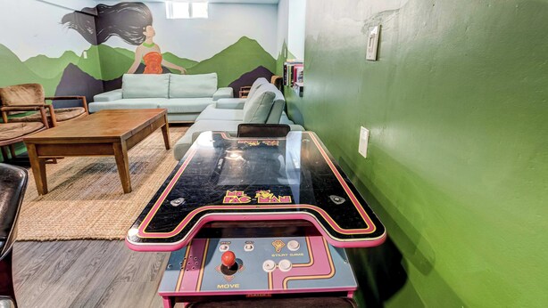 A room with a green wall, a sofa, a coffee table, and a pinball machine. - Aloha Springs! Private Heated Pool & Hot Tub (Colorado Springs)