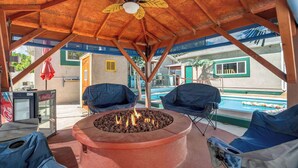 An outdoor seating area with a fire pit, covered by a wooden structure with a leaf-shaped ceiling fan. - Aloha Springs! Private Heated Pool & Hot Tub (Colorado Springs)